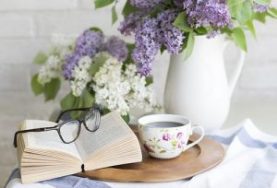 kleiner Tisch mit Teetasse, Vase mit Flieder, Buch und Brille